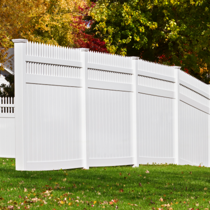 White vinyl fence with ornate picket details on the top amidst the colorful leaves of autumn trees
